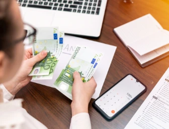 Žena sedící u stolu a počítající zisky u svého počítače